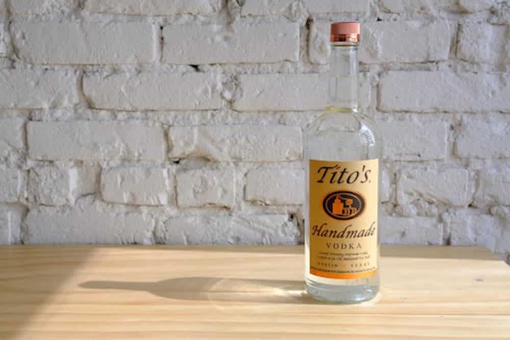 Bottle of Tito's handmade vodka on wooden table with brick background