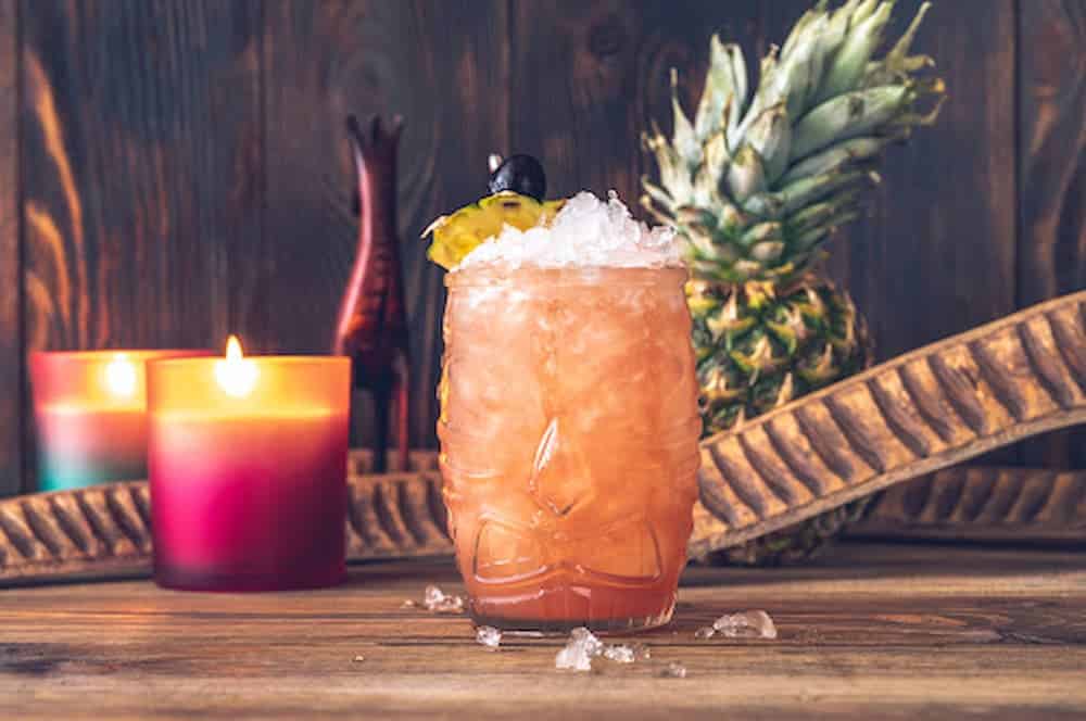 Cocktail in glass filled with ice with pineapple and candles in background