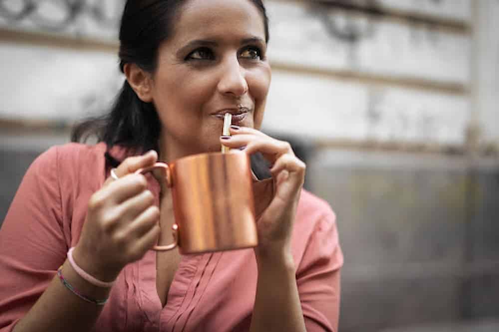 Ethnic-woman-sipping-out-of-copper-mug-with-straw