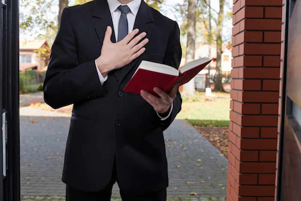 Jehovahs-Witness-wearing-black-suit-standing-at-door-holding-a-Bible