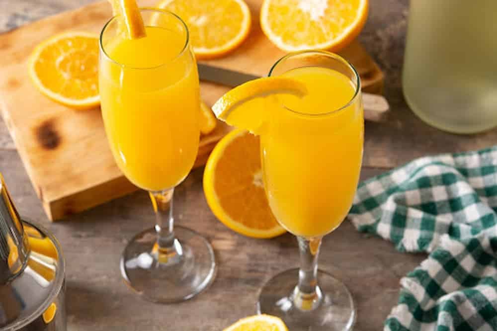 Mimosas in flute glasses with orange slices in background
