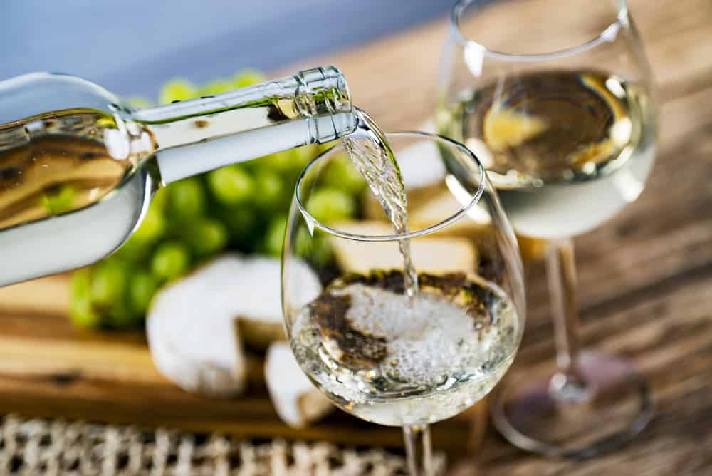 Pouring white wine into a clear wine glass with charcuterie board in background