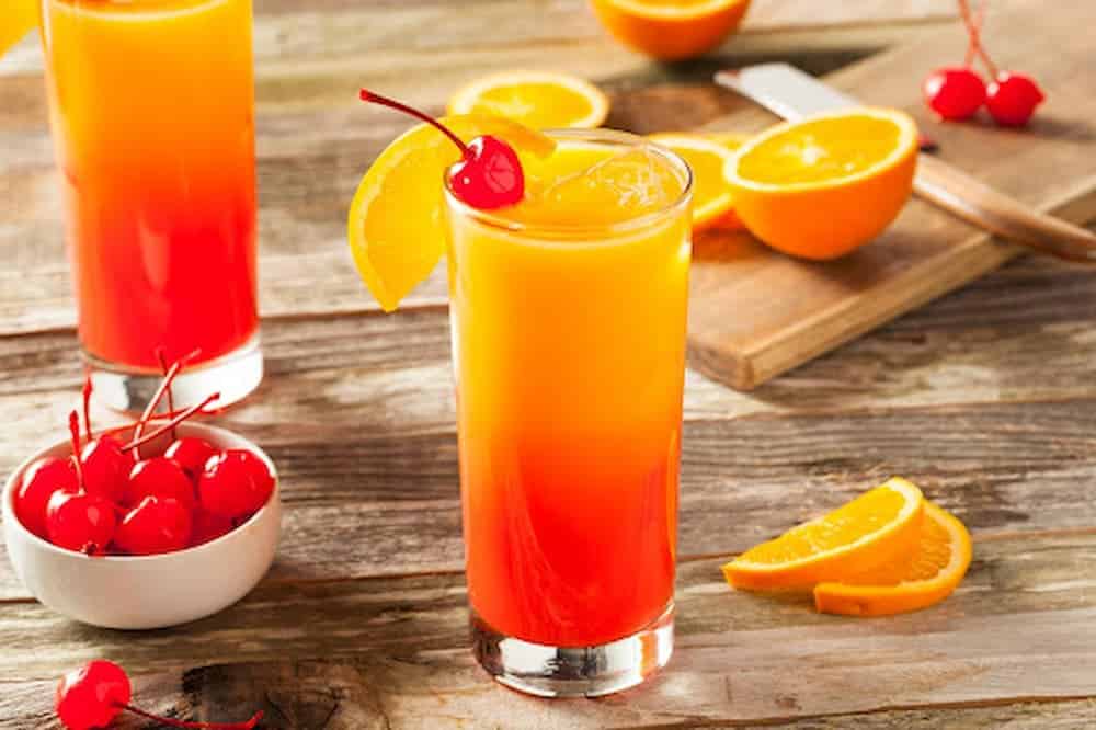 Tequila Sunrise drinks in tall glasses with cherries and orange slices